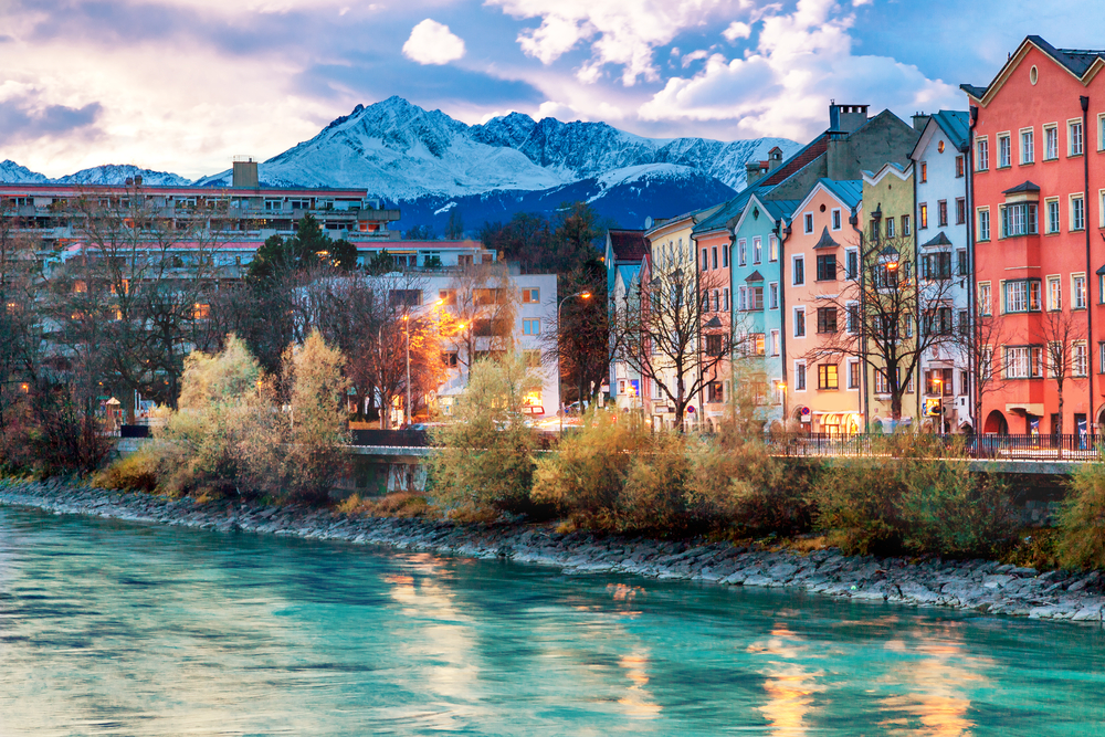 Ez a kép az ausztriai Innsbruck városát ábrázolja, az Inn folyó mentén sorakozó színes házakkal és a Nordkette-hegység hófödte csúcsaival a háttérben - Z(s)eppelin utazás